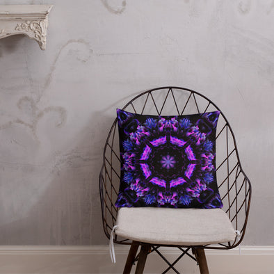 Photograph of a model wearing Bleace unisex MetaParty Vibes Kaleidoscopic purple, blue, and pink, Trippy Visual pillow placed on a chair in the foreground with a grey wall background.  